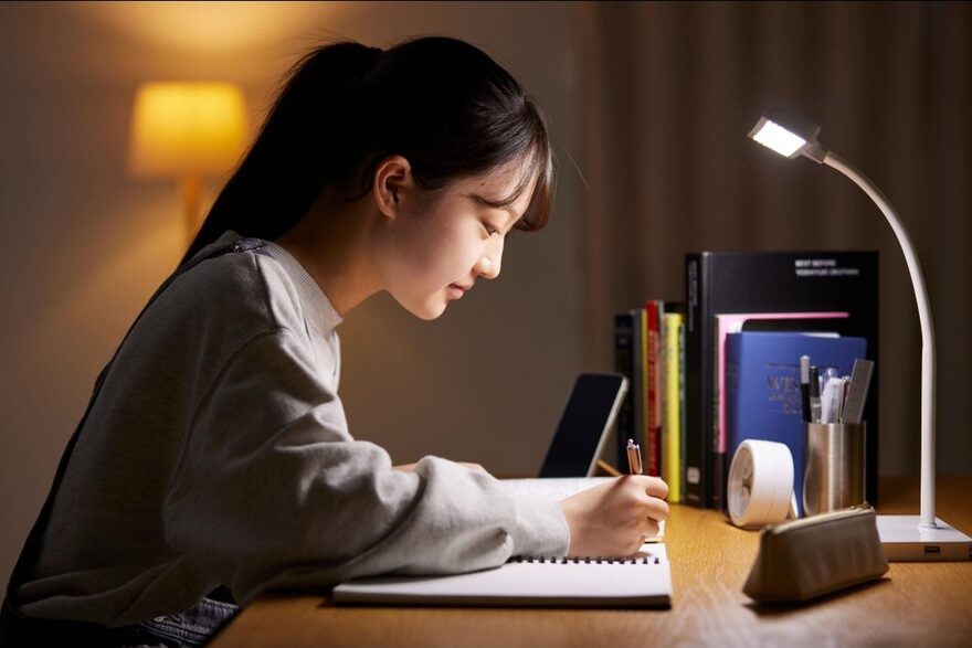 A student studies with focus at a desk lamp, building daily test-prep discipline.
