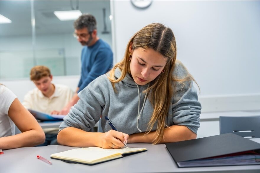 A student writes while a teacher supports nearby, like MyTutor guiding every step.